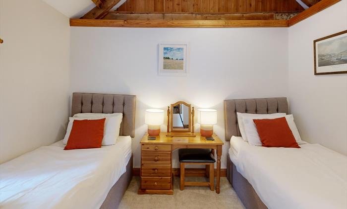 Twin beds with burnt orange cushions and a central dressing table beneath sloped ceiling and beams.
